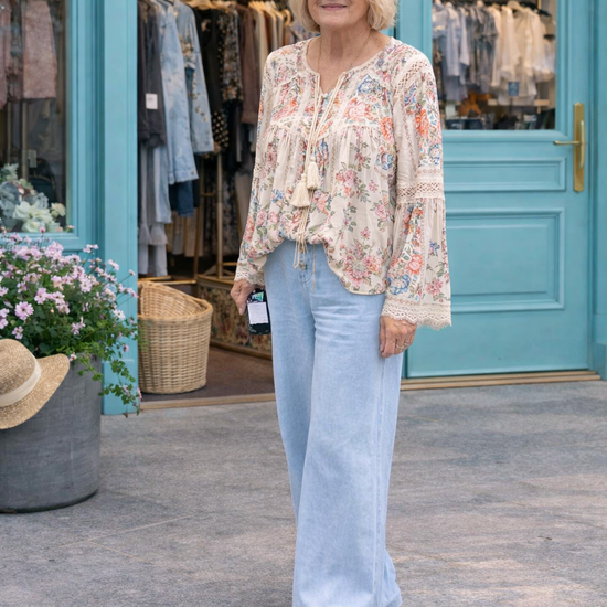woman wearing light wash wide leg denim pants with flowy boho blouse styled outside boutique with turquoise doors